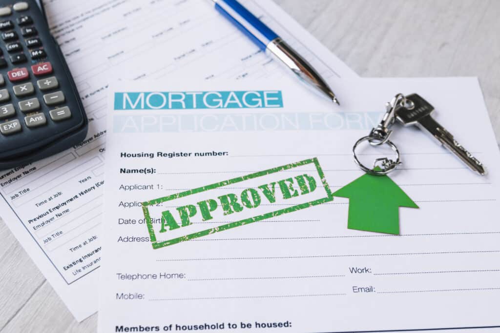 A mortgage application form marked APPROVED with a green stamp, a pen, a calculator, and house keys with a green house-shaped keychain on a desk&mdash;highlighting the option to avoid foreclosure or consider alternatives like a short sale.