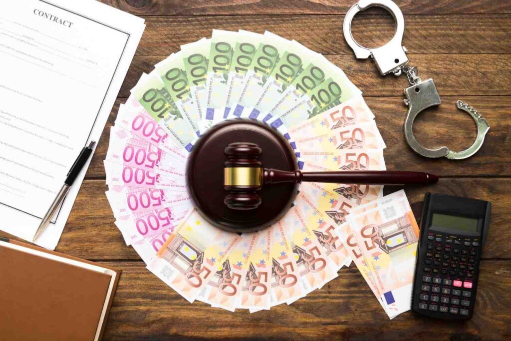 A judge’s gavel rests on a circle of Euro banknotes, surrounded by handcuffs, a contract, a wage garnishment calculator, and a notebook on a wooden table.