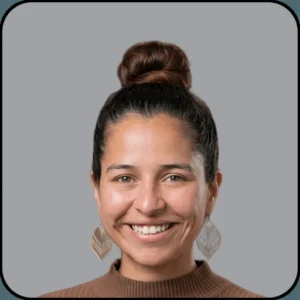 A woman with dark hair in a high bun, wearing large, patterned earrings and a brown turtleneck sweater, smiles at the camera against a plain gray background.